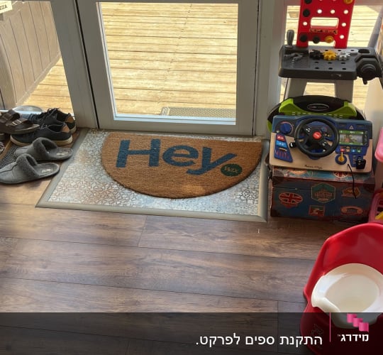 רצפת פרקט חומה ליד דלת זכוכית עם שטיחון "Hey".